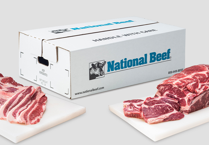 Two raw beef cuts displayed on white boards with a white National Beef shipping box behind them.