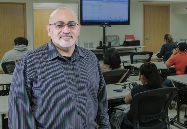A man standing in front of a classroom of adult students with a projector screen behind him.