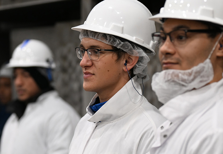 安全ヘルメットと白衣を着用した従業員が作業エリアに並んでいます。
