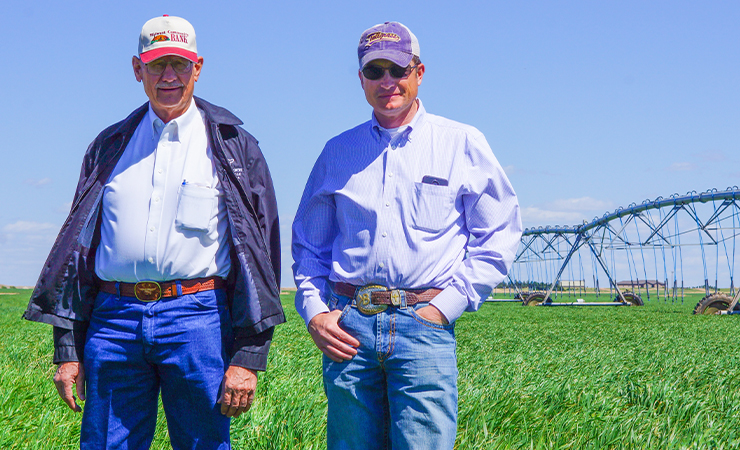 Two men standing in a lush green field with irrigation equipment in the background.