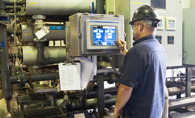 Worker operating industrial equipment and monitoring a digital control panel inside a facility.