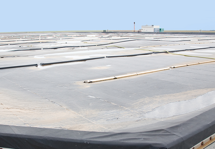 Large covered wastewater treatment pond with pipes and equipment visible across the surface.