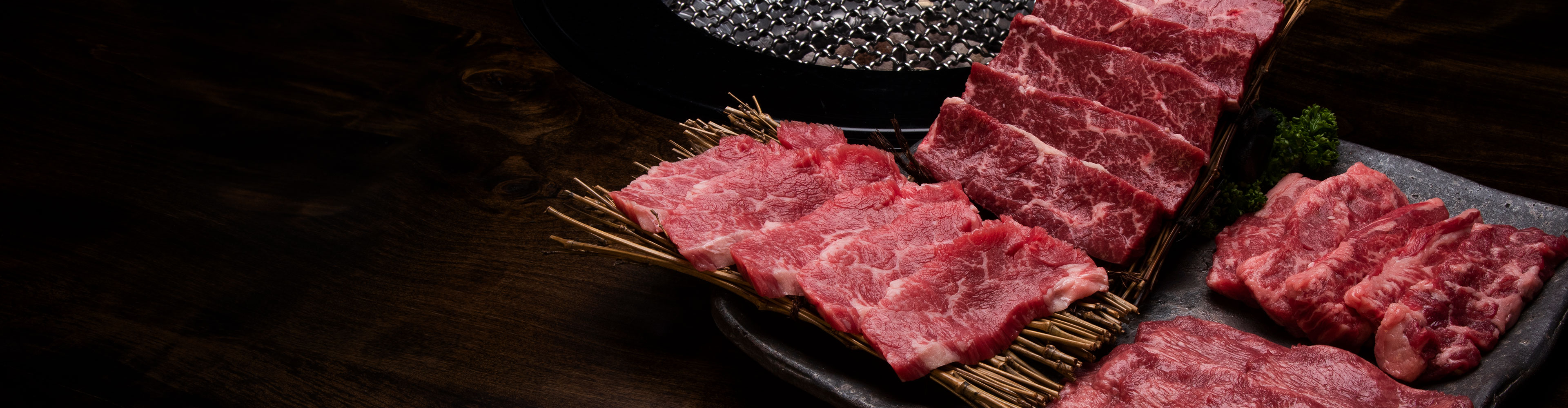 生の牛肉の切り身が、付け合わせとともに黒い石の皿の上にグリルの横に並べられています。