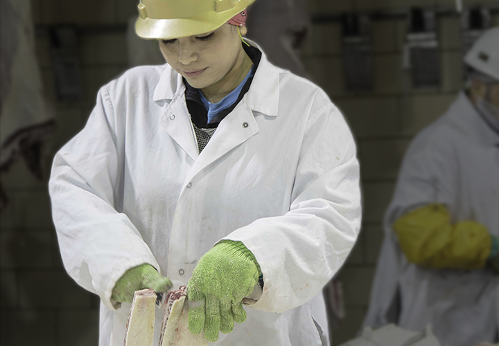 Worker in protective gear trimming a beef cut on a processing line.