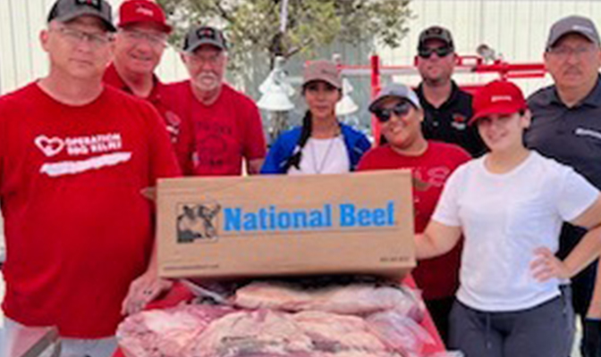 Group of people at an outdoor community event standing behind a table of packaged beef with a National Beef box.
