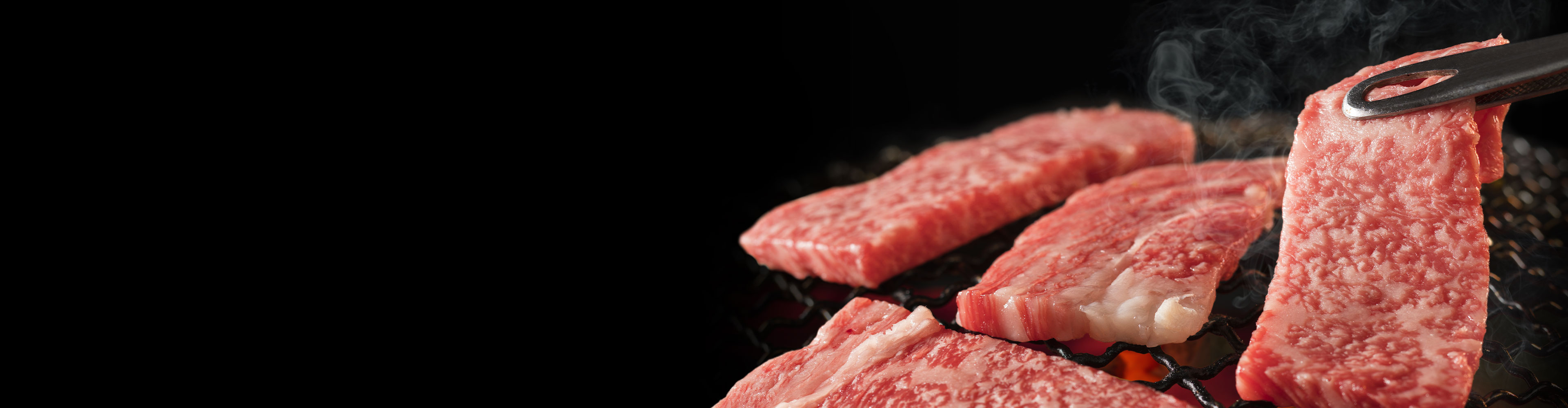 薄く霜降りになった牛肉のスライスを、トングで一枚ずつ持ち上げて直火で焼いています。
