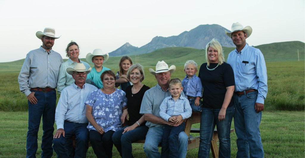 Group photo of a multi-generational ranching family posing outdoors in a grassy landscape with hills in the background.