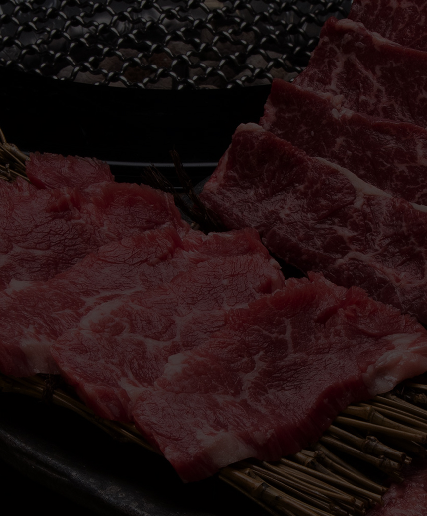 生の牛肉の切り身が、付け合わせとともに黒い石の皿の上にグリルの横に並べられています。