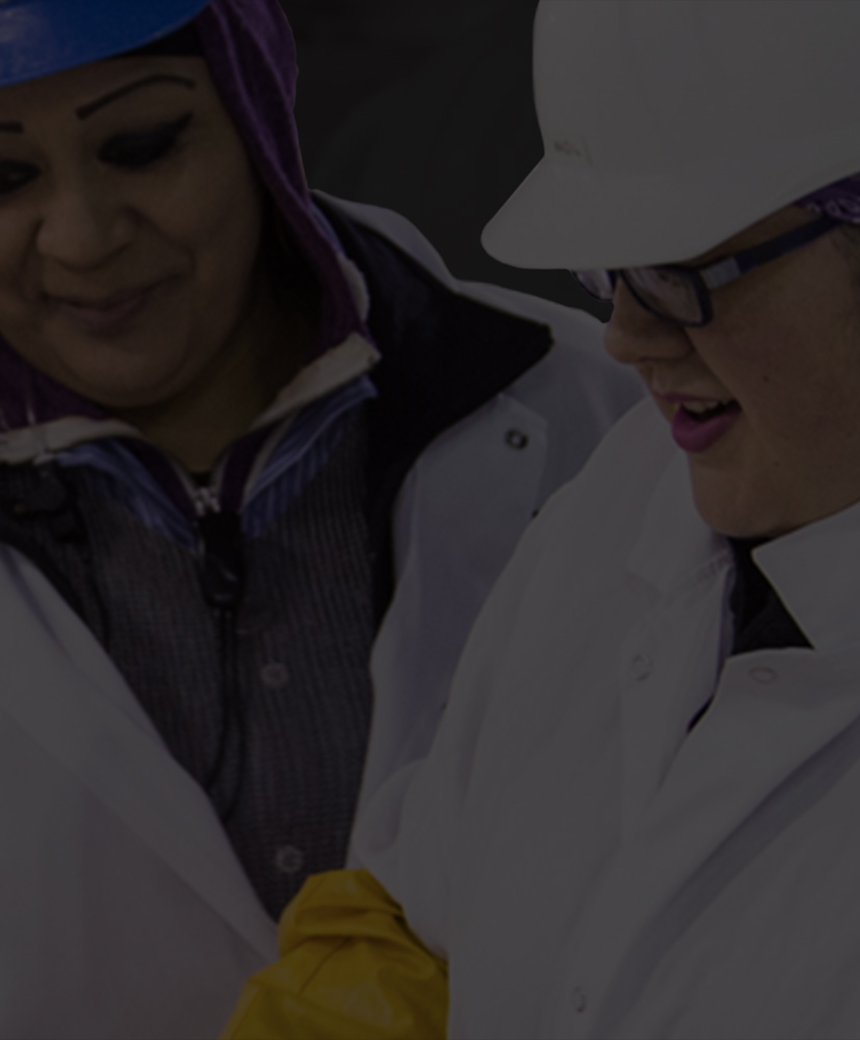 Two production workers in protective gear smiling and talking while processing beef on the factory floor.