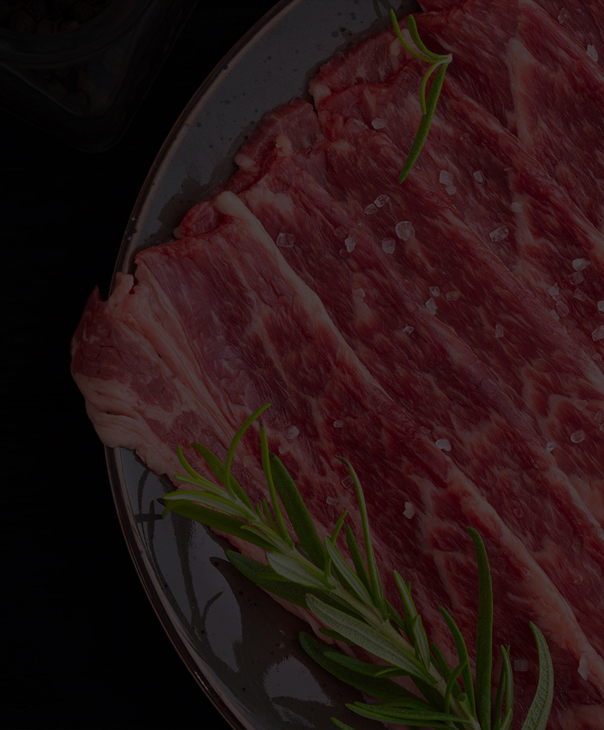 Raw beef slices arranged on a plate with rosemary and seasonings on a dark background.