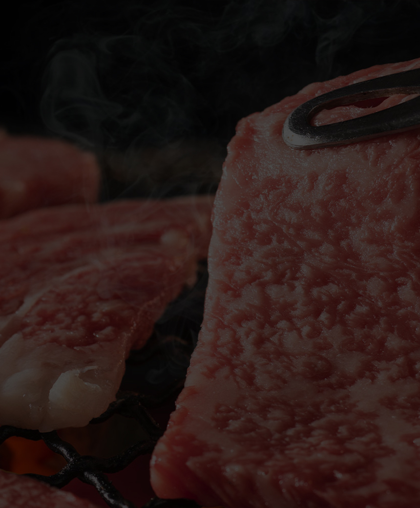 Thin, marbled beef slices grilling over open flames with tongs lifting one slice.
