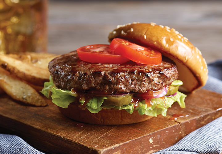 Close-up of a hamburger with lettuce on a sesame bun, served with fries and dipping sauce.