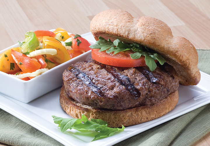Grilled beef burger on bun with tomato and side of mixed peppers on white plate