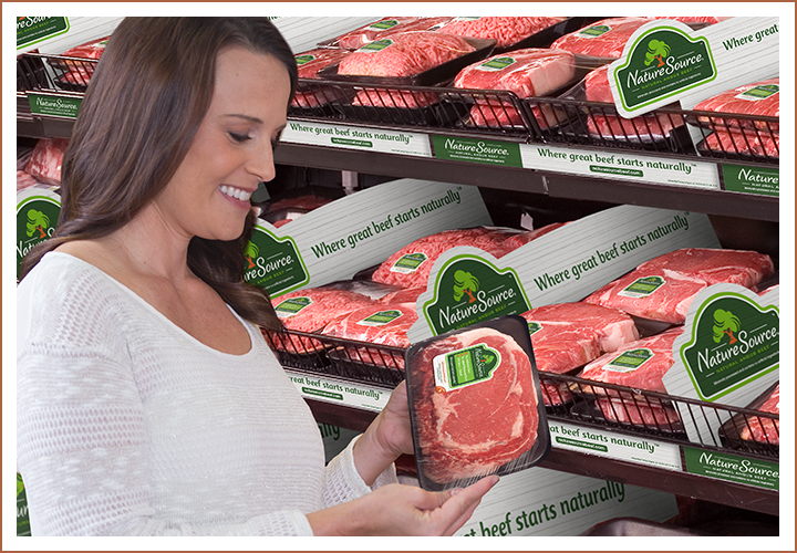 Woman shopping in grocery store meat aisle, smiling while holding packaged steak labeled NatureSource