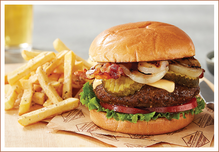 Cheeseburger with bacon, grilled onions, pickles, and fries on a wooden board