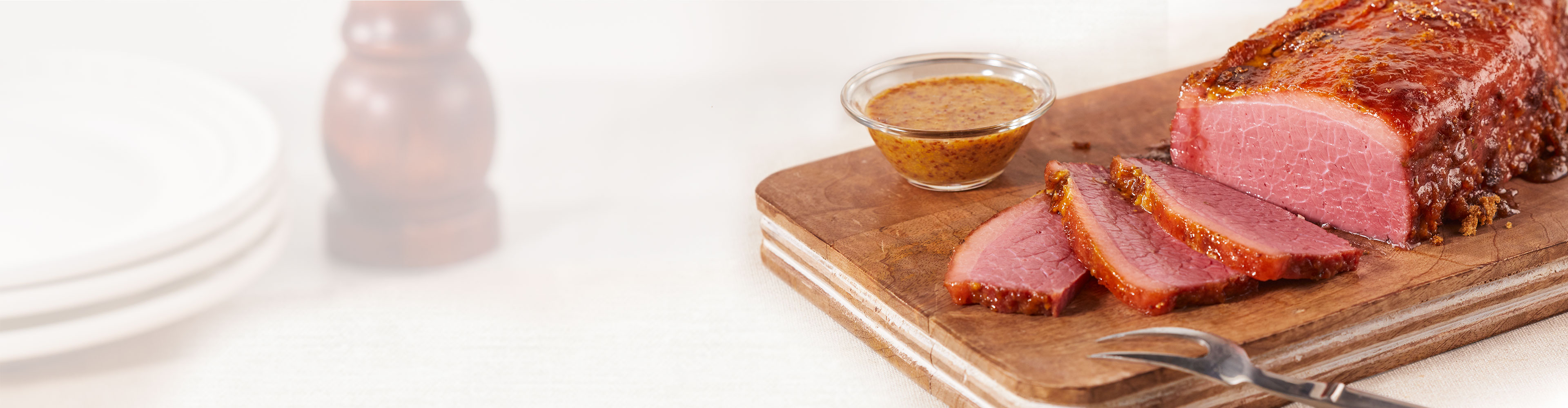 Sliced corned beef on a cutting board with a small bowl of mustard sauce.
