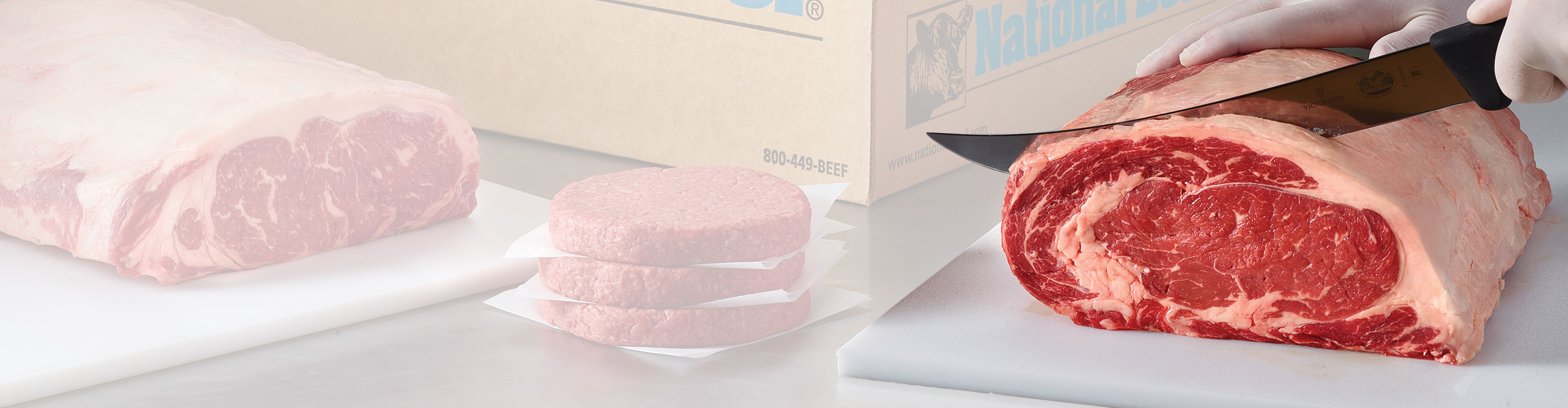 Person slicing a large ribeye primal beside stacked beef patties and a National Beef box.