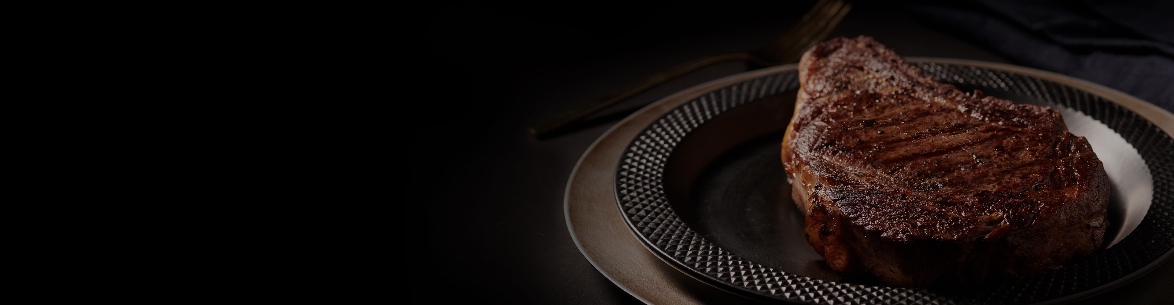 Grilled steak on a decorative plate against a dark background.