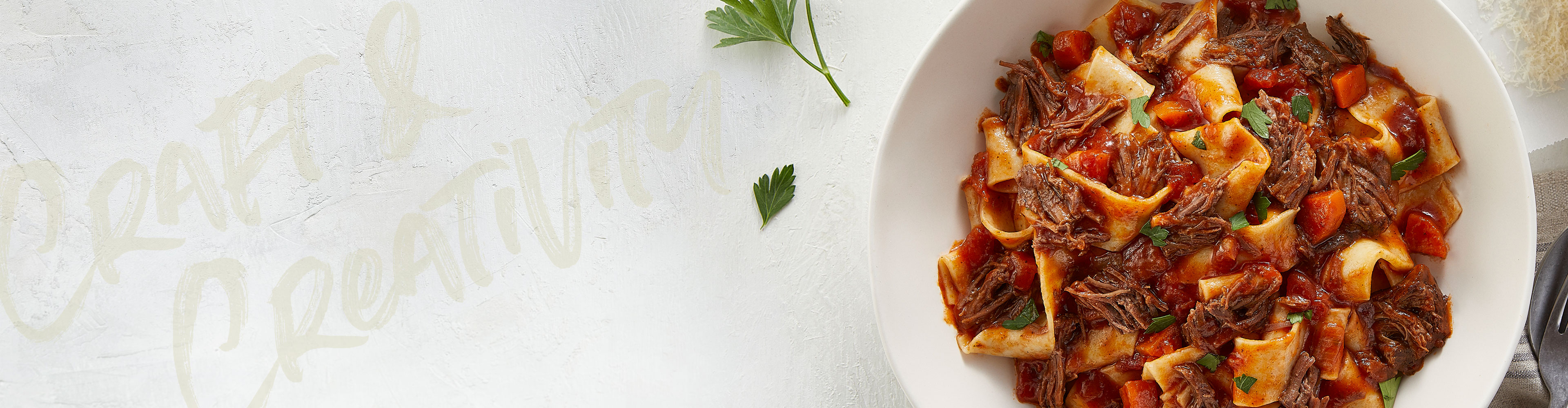 Bowl of pasta with shredded beef and tomato sauce garnished with herbs.