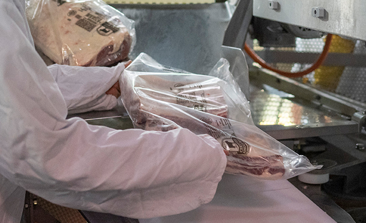 Worker in a white coat loads vacuum-packed Certified Angus Beef cuts into packing equipment
