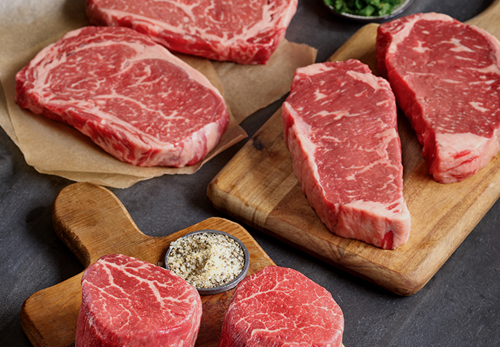 Assorted raw steaks on cutting boards with herbs and seasonings.