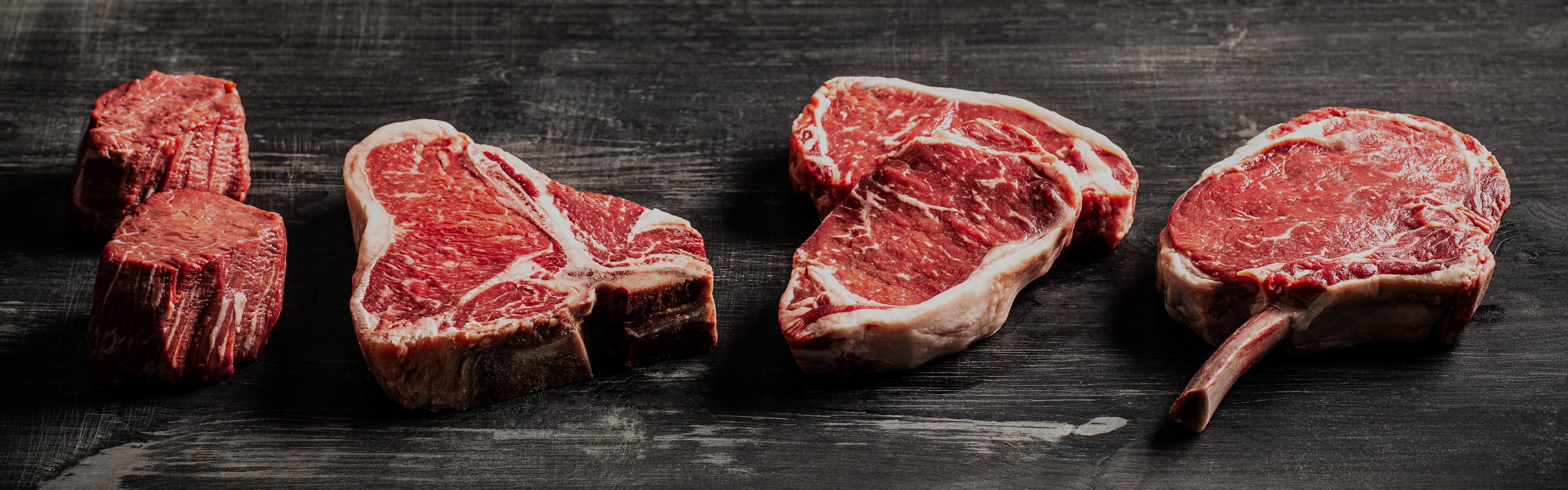 Row of assorted raw beef cuts lined up on a dark wooden surface