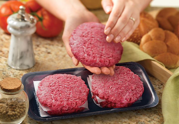 Hands placing a raw ground-beef patty onto a tray holding two patties.