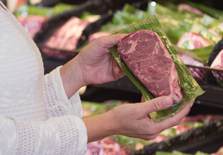 Woman inspecting a packaged beef steak in a grocery meat department.
