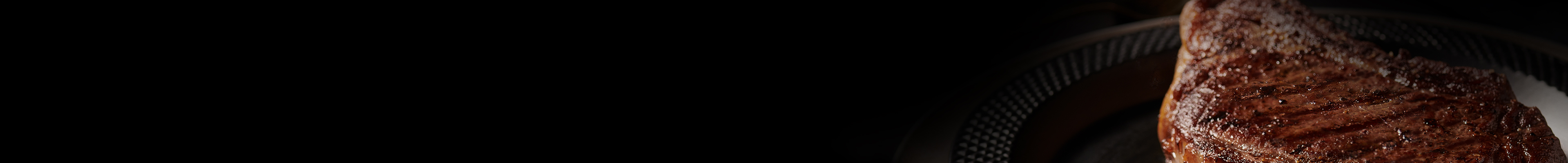 Grilled steak on a dark plate with a black gradient background.