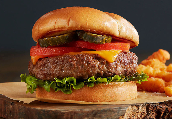Close-up of a cheeseburger with lettuce, tomato, pickles, and a side of crinkle-cut fries.