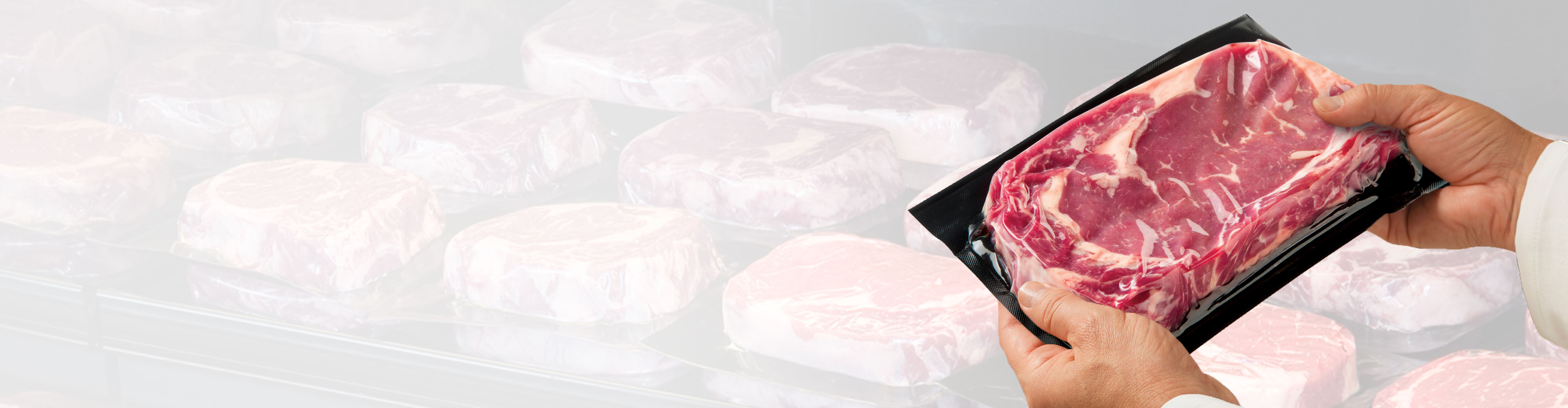 Person holding a vacuum-sealed steak in front of a display case filled with packaged steaks.
