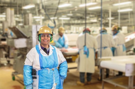 Worker wearing protective gear and a gold hard hat smiling in a food processing facility
