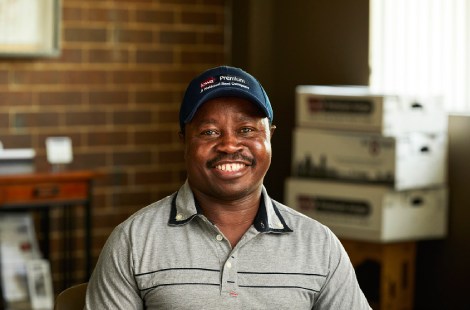 Smiling worker wearing an Iowa Premium cap seated indoors with boxes in the background