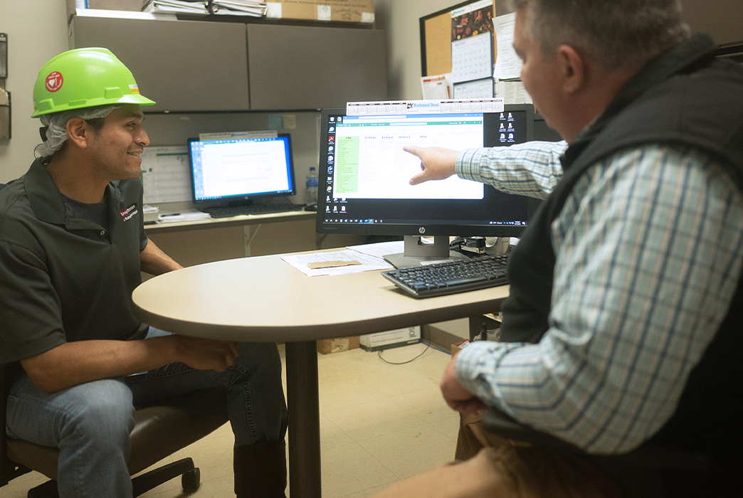 wo employees discussing something on a computer screen in an office.