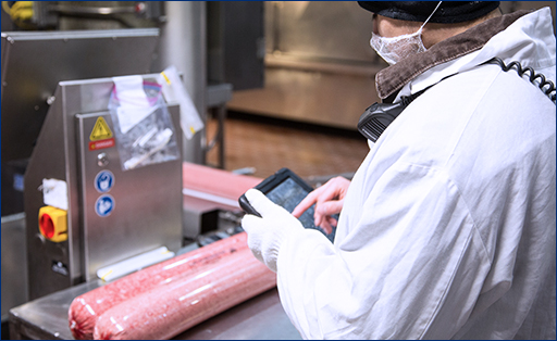 Factory worker in protective gear checking packaged ground meat.