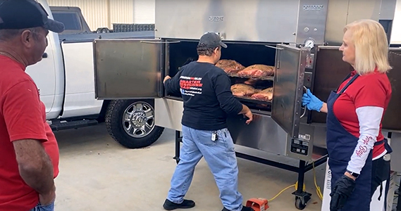 Group preparing meat at an outdoor smoker.