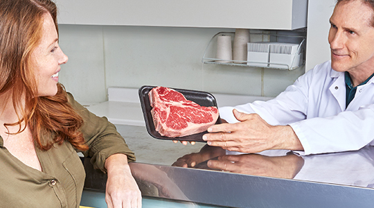 Butcher handing packaged meat to a smiling customer across a counter.