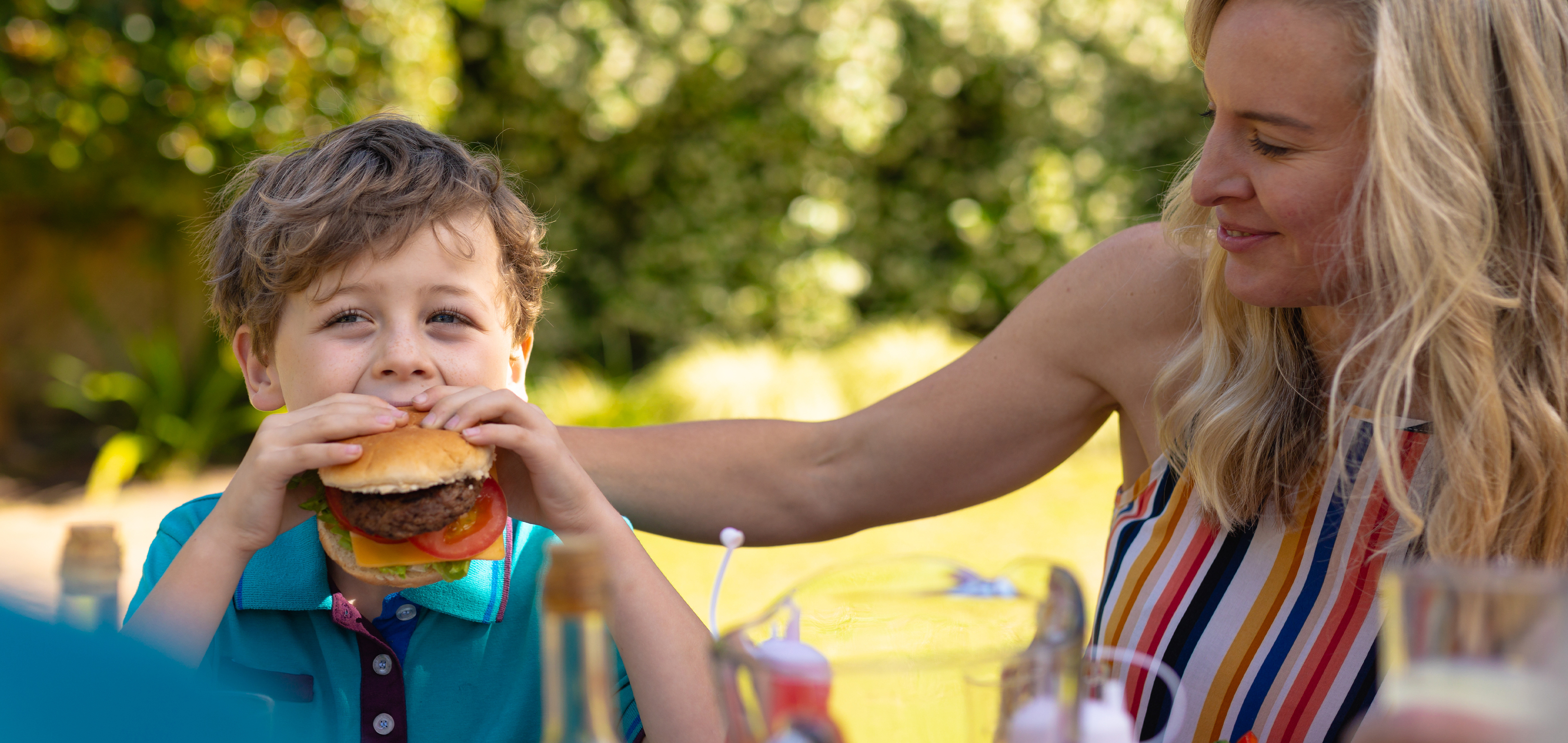 Mother and child at a picnic while eating burgers.