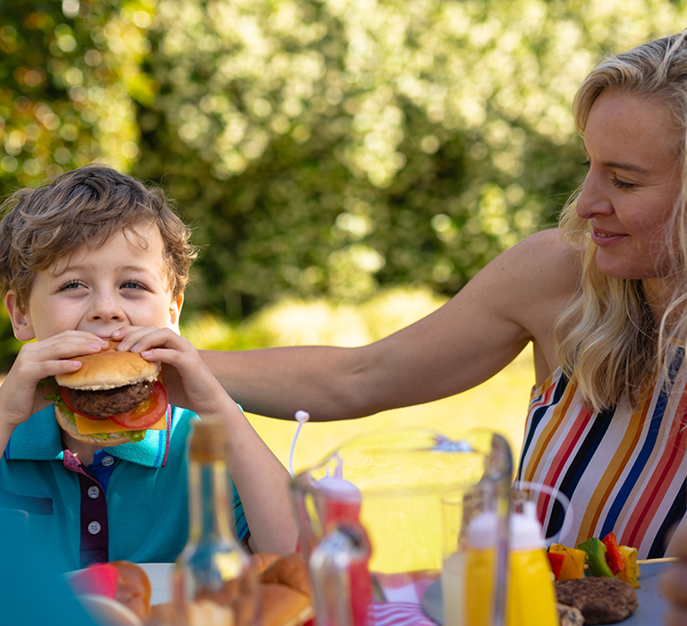 Mother and child at a picnic while eating burgers.