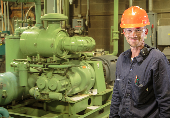 Industrial worker in safety gear standing near machinery.