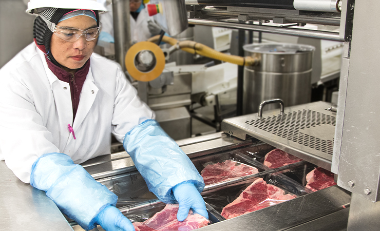 Employee sealing packaged meat in machinery.