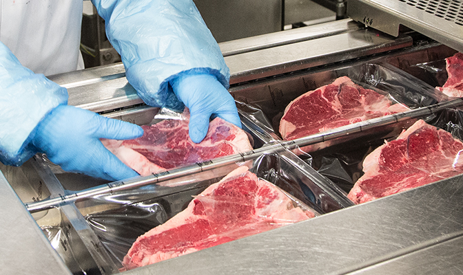 Employee placing packaged steaks in sealing machine.