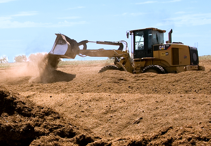 Bulldozer lifting and moving soil at an agricultural site.