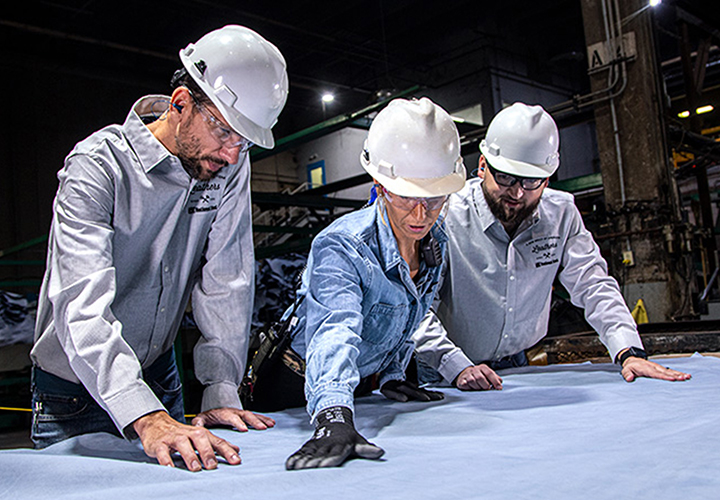 Three workers in safety gear examining material on a table.