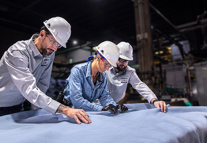 Team in hard hats inspecting a large sheet of leather.