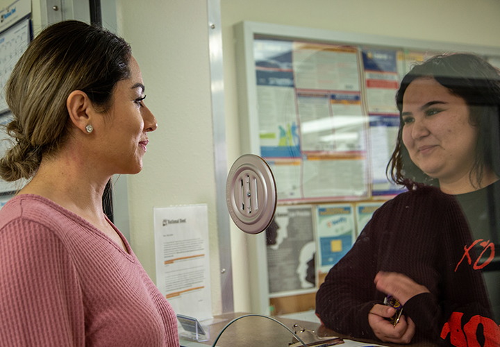 Two women talking through a glass window at a workplace office.