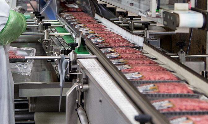 Packaged ground beef moving through automated line.