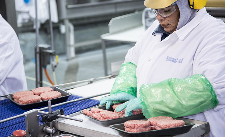 Employee inspecting hamburger patties on conveyor belt.