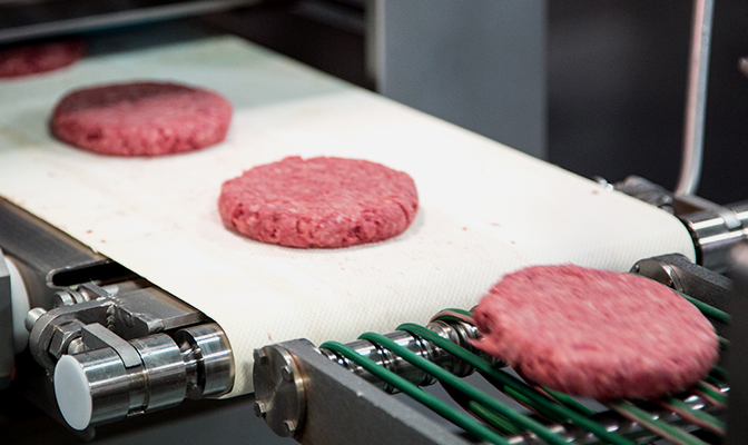 Beef patties traveling on conveyor in production area.