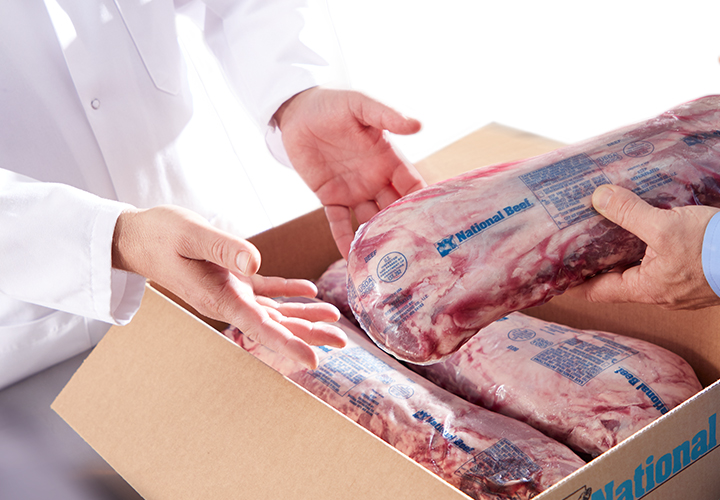 Worker placing packaged beef cuts into a National Beef box.
